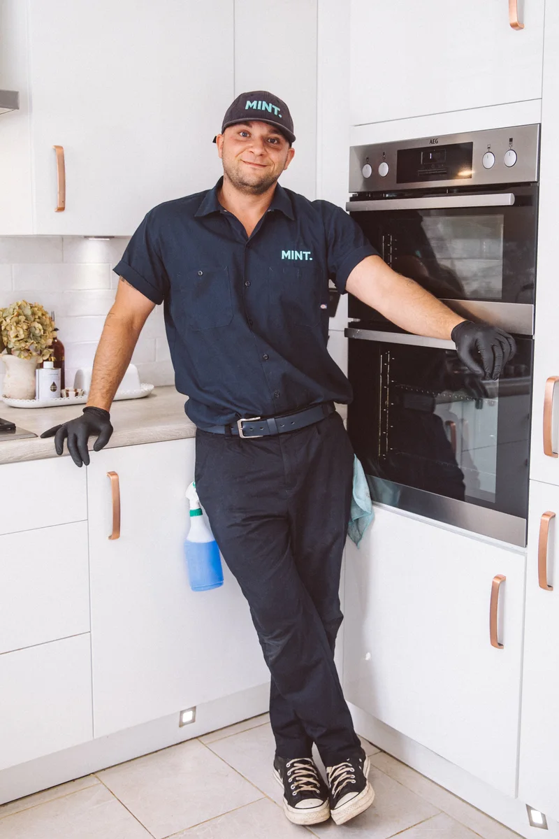 Taylor in his MINT uniform standing beside an oven in a kitchen